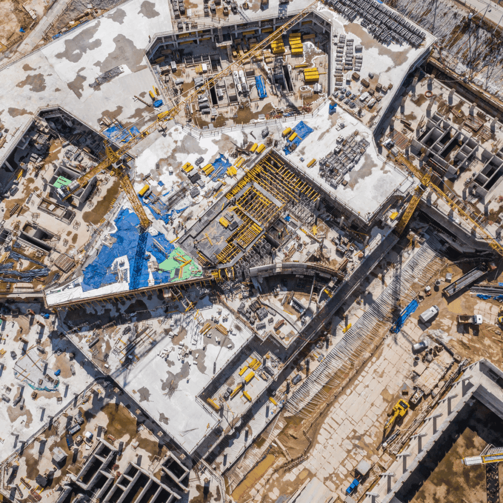 Aerial view of a construction site with cranes, scaffolding, and tarp-covered sections, highlighting organized equipment access.