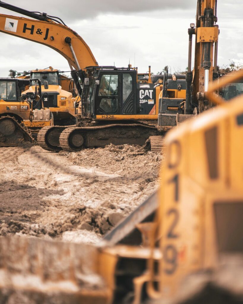 Large yellow excavators and CAT construction vehicles work on a muddy site under cloudy skies, illustrating a connected jobsite.