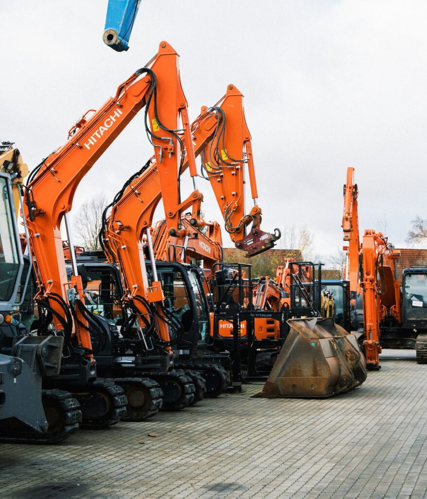 A row of bright orange Hitachi excavators with raised arms is parked on a lot, showing construction equipment and fleet management.