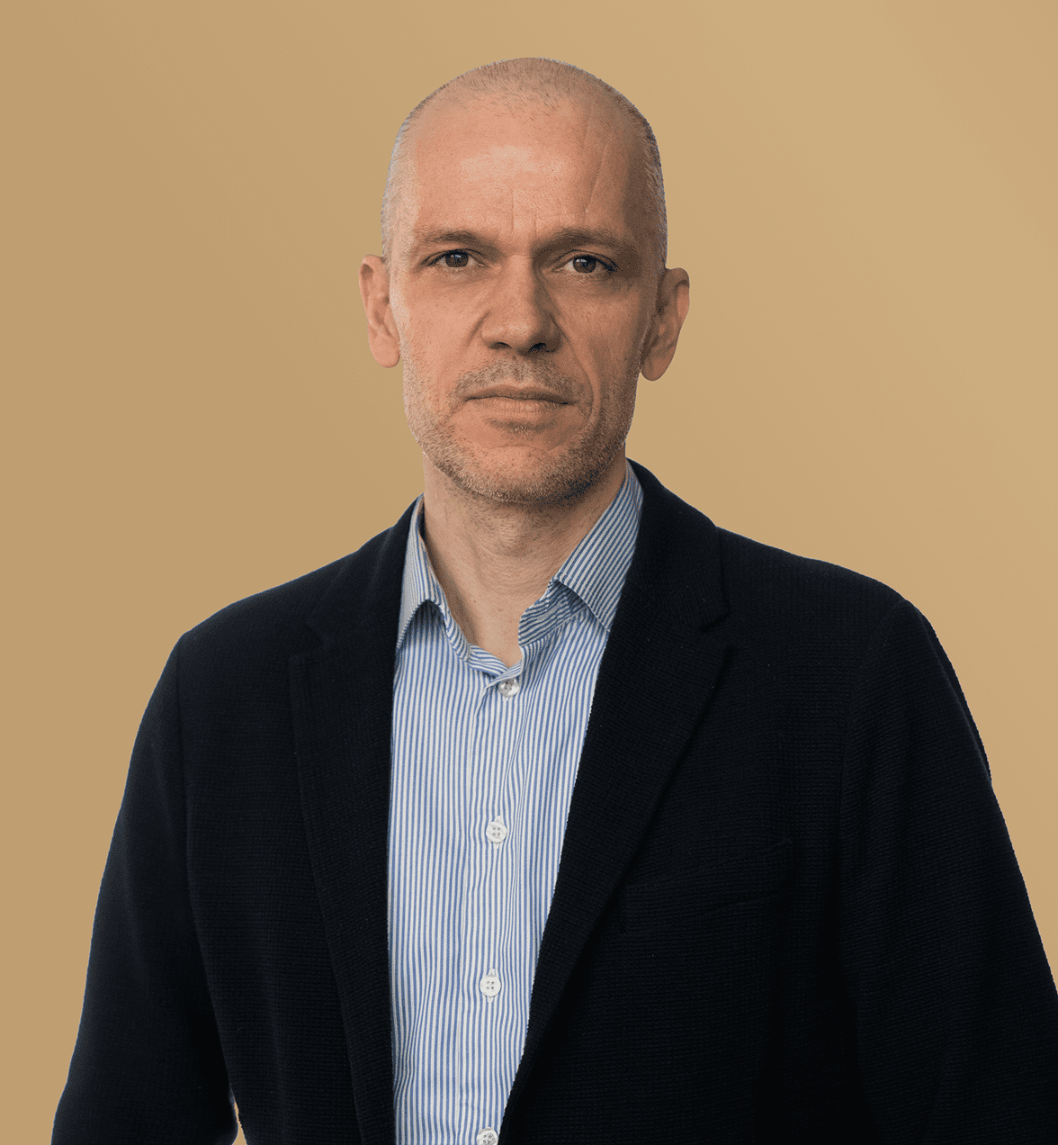 A middle-aged man with a shaved head in a blazer and striped shirt stands against a beige background, linked to construction equipment tracking.