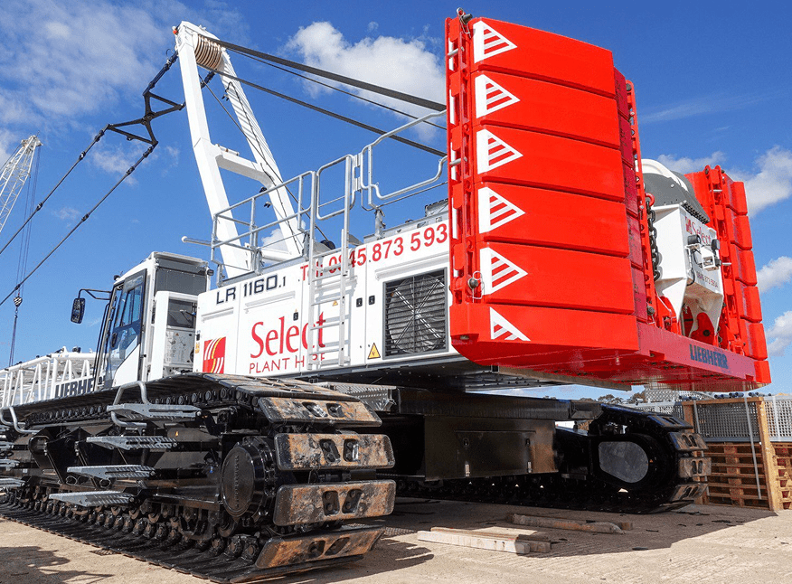 A large white and red tracked construction crane with Select Plant Hire branding is parked on a concrete surface under a blue sky with scattered clouds. The crane has a prominent red counterweight section.