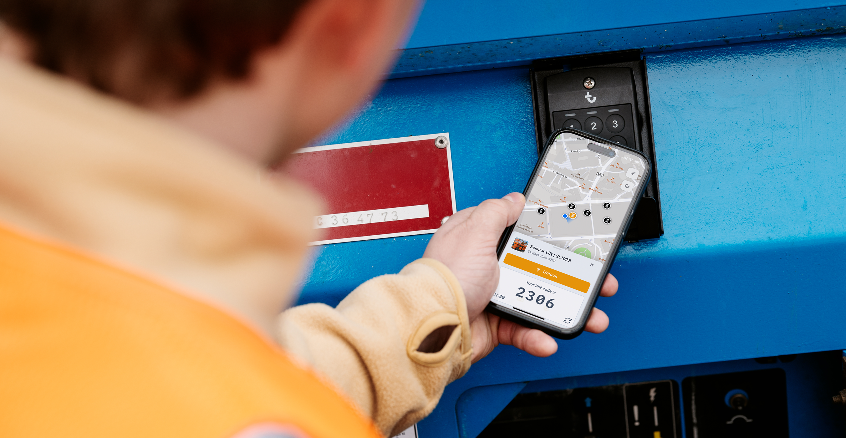 A person in a yellow safety vest uses a smartphone with a map app next to a blue machine, illustrating construction equipment tracking.