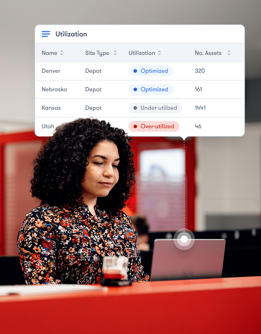 A woman with curly hair uses a laptop beneath a digital table showing depot utilization and asset data, linked to fleet management.