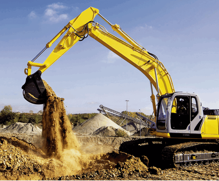 A yellow excavator with aftermarket parts moves dirt at a construction site, surrounded by equipment and earth under a blue sky.