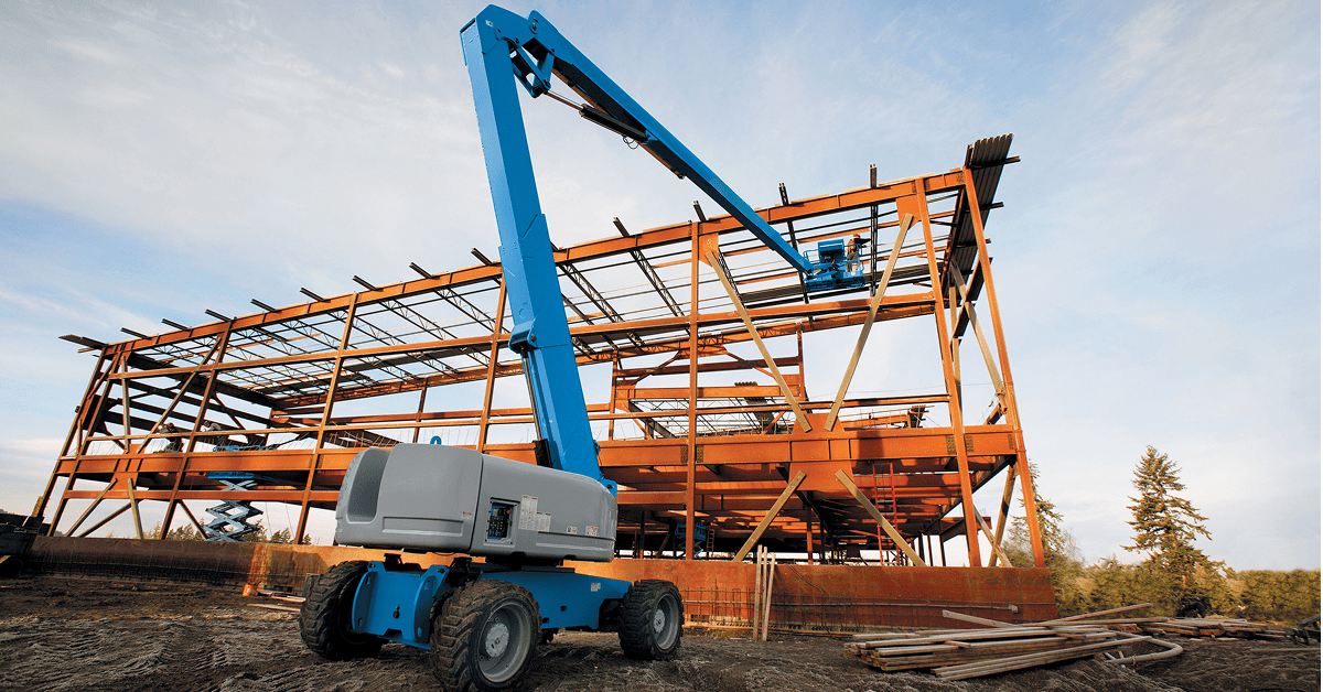 A blue boom lift works by a steel building frame at a connected jobsite, with scattered materials and trees in the background.