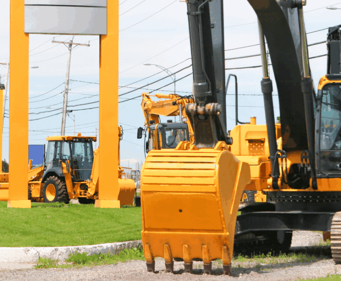 Yellow construction vehicles, including an excavator and loaders, are parked on gravel near a street—fleet management.