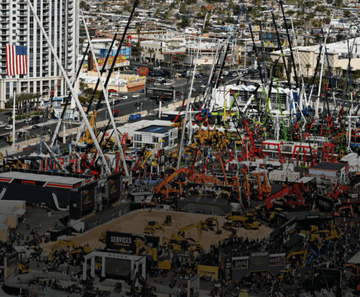 Cranes and machinery on display at bauma 2025 outdoor expo, with crowds and city buildings; highlights construction equipment tracking.