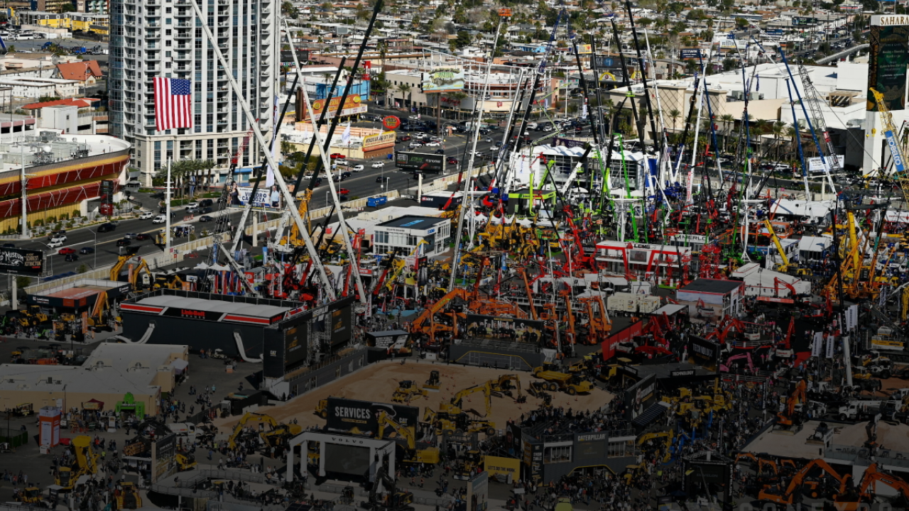 Cranes and machinery on display at bauma 2025 outdoor expo, with crowds and city buildings; highlights construction equipment tracking.