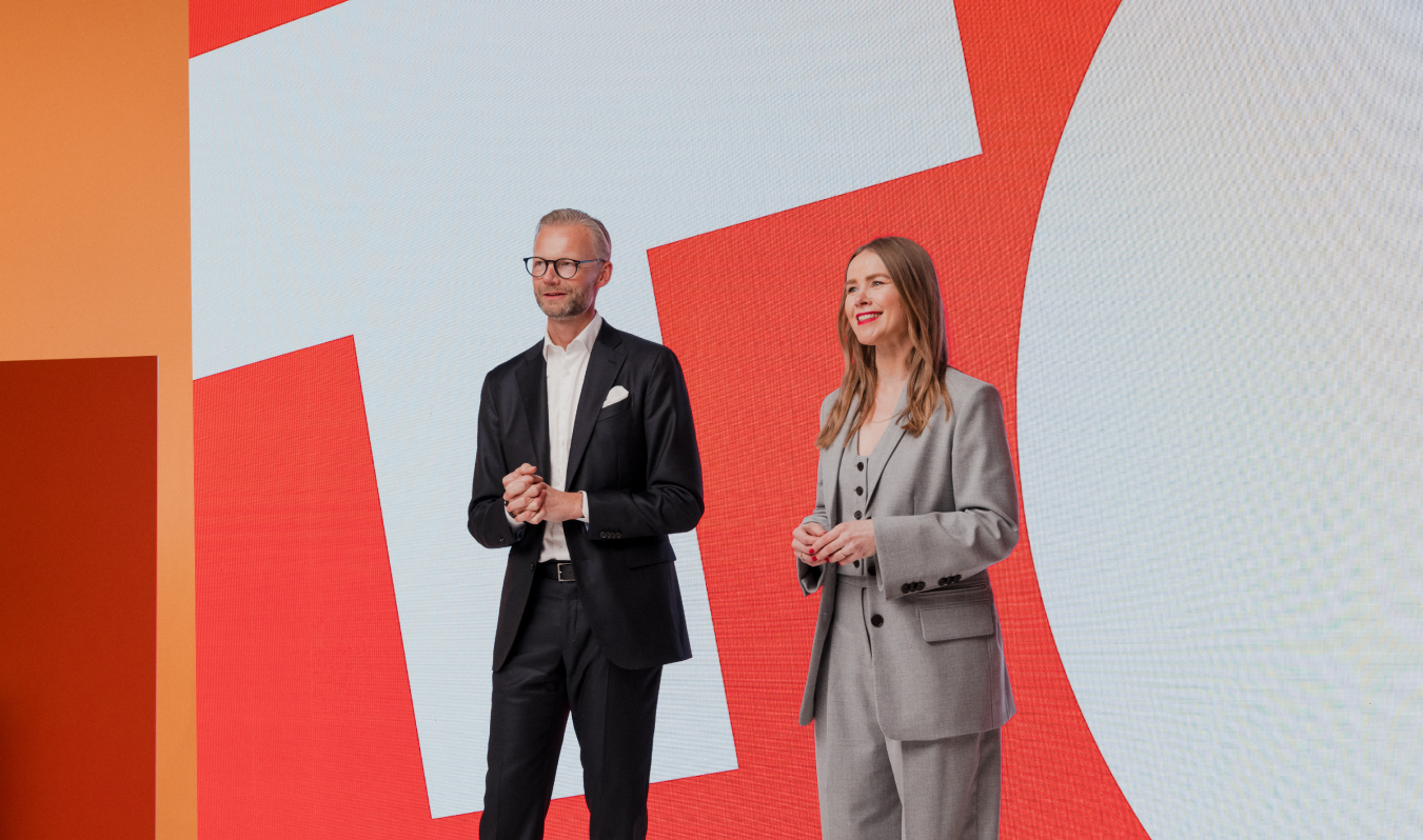 Two people present on stage at Trackunit Next, smiling in front of a vibrant geometric backdrop related to construction IoT.