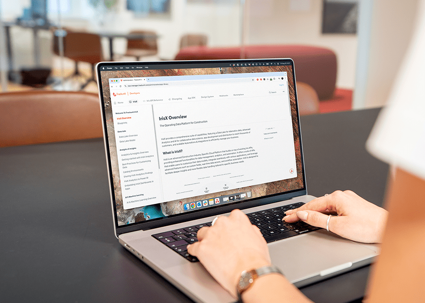 Person typing on a laptop showing Ink Overview, seated at a black table in a modern office related to connected jobsite solutions.