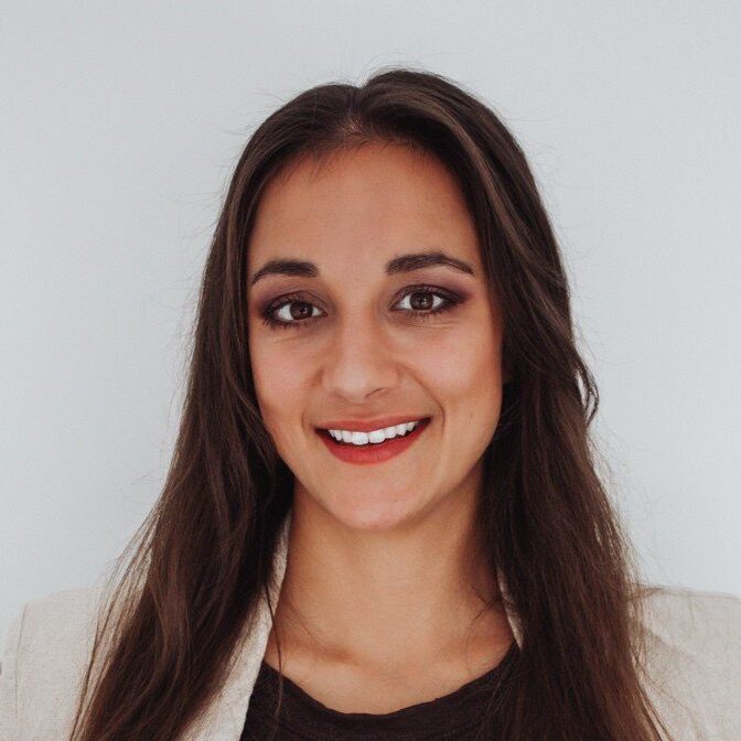 A woman with long brown hair in a beige blazer smiles at the camera, reflecting a professional vibe for construction equipment tracking.