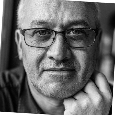 Black-and-white close-up of a middle-aged man with glasses, looking thoughtful—a nod to construction equipment tracking precision.