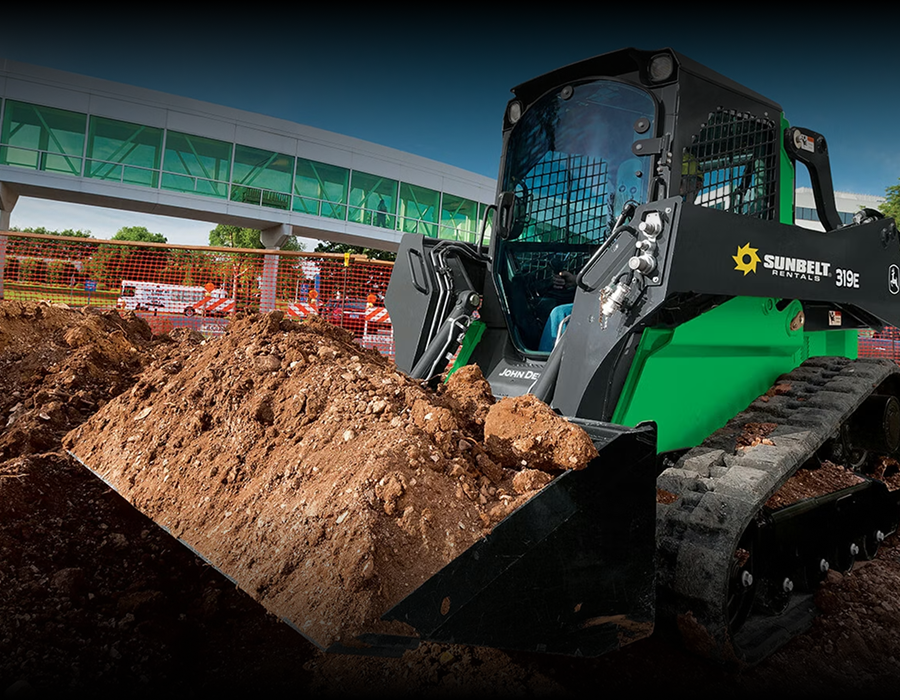 A green and black Sunbelt Rentals skid steer loader moves dirt at a construction site, part of a connected jobsite.