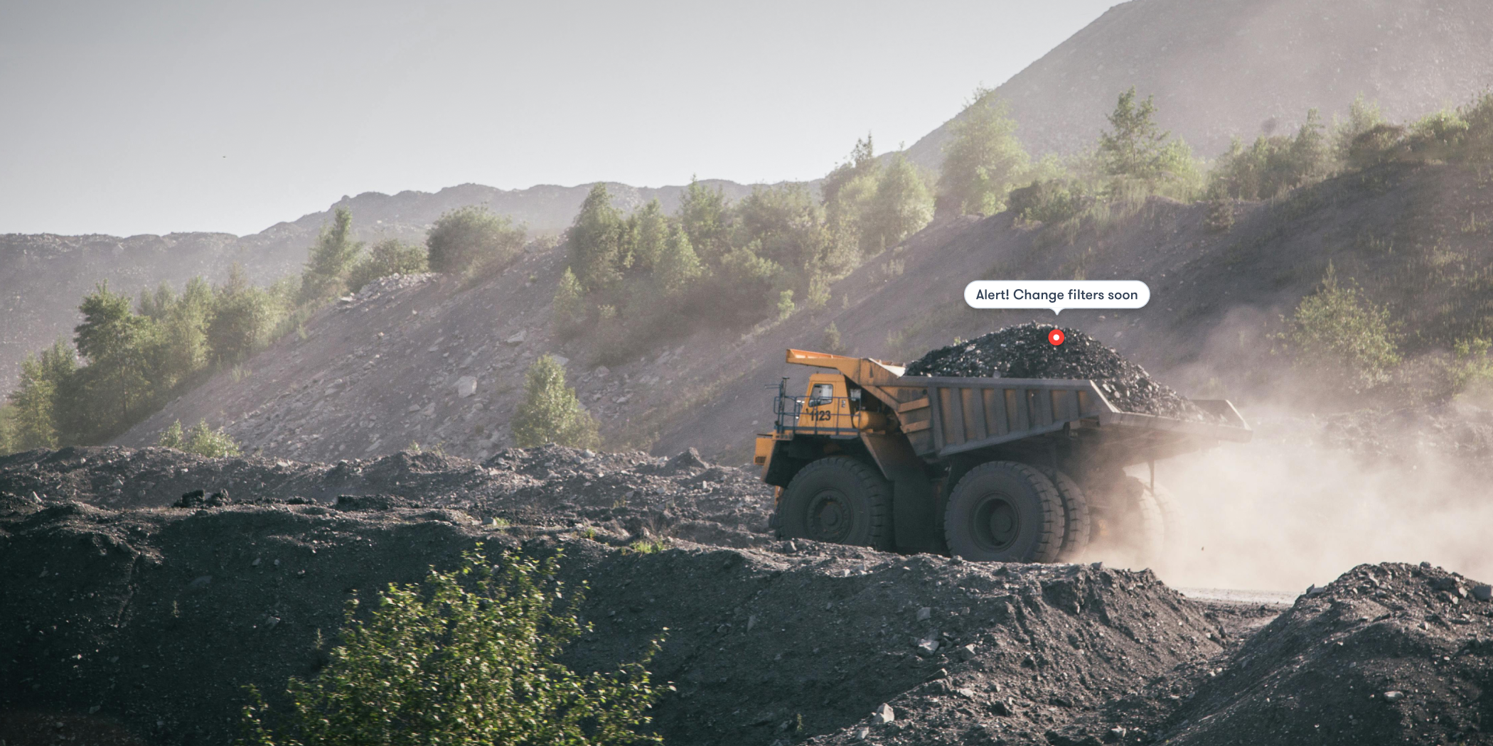 A mining dump truck hauls coal through dusty terrain as a Construction AI alert says, “Alert! Change filters soon.” Fleet management.