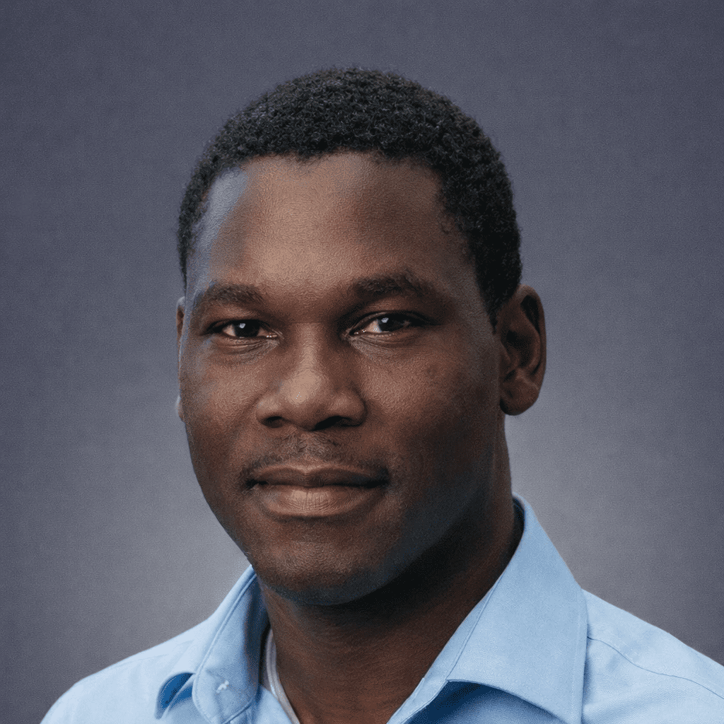 A man with short curly black hair in a light blue collared shirt smiles slightly against a calm grey background, ideal for connected jobsite.