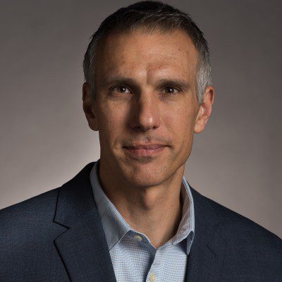 A middle-aged man with short gray hair in a blue blazer poses confidently, reflecting IrisX’s professionalism in construction IoT.