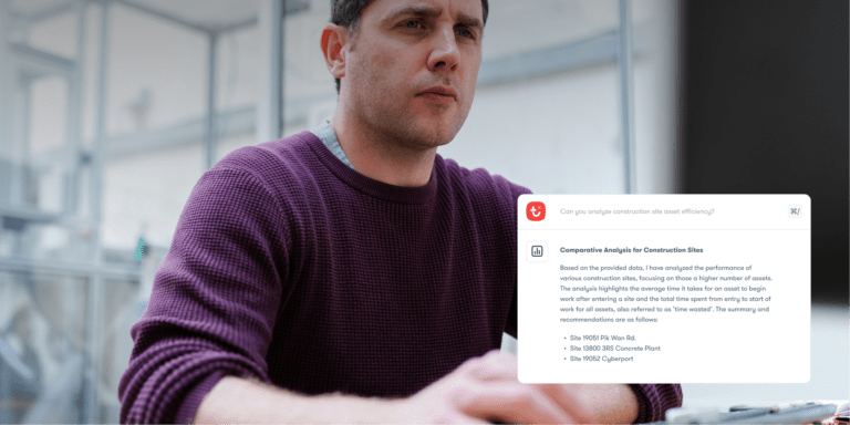 A man in a maroon sweater reviews a computer screen showing a construction site report and recommended installs, highlighting connected jobsite.