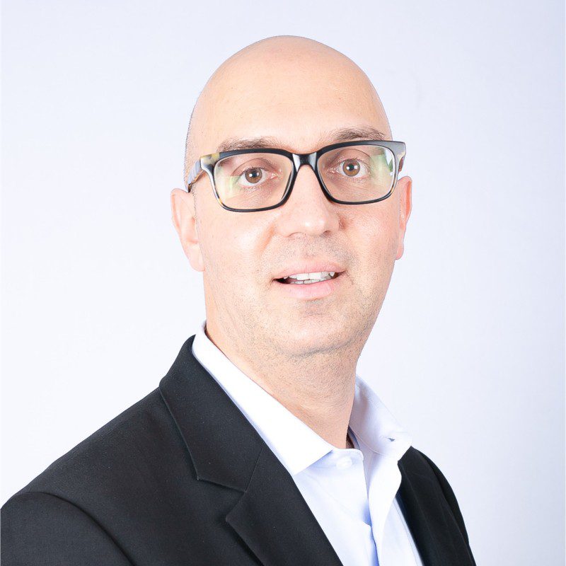 A man with a shaved head and glasses in business attire, smiling slightly at the Downtime Summit focused on construction IoT.