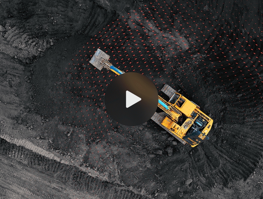 A yellow excavator on dark soil at a construction site with red marker flags and a play button overlay, showing fleet management.