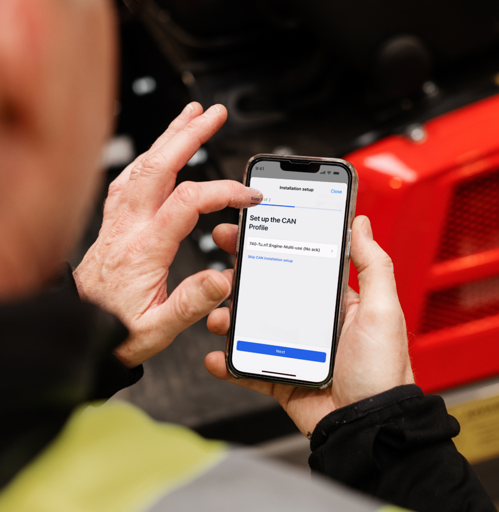 A person in a high-visibility jacket installs a CAN profile on a smartphone app, supporting construction equipment tracking.