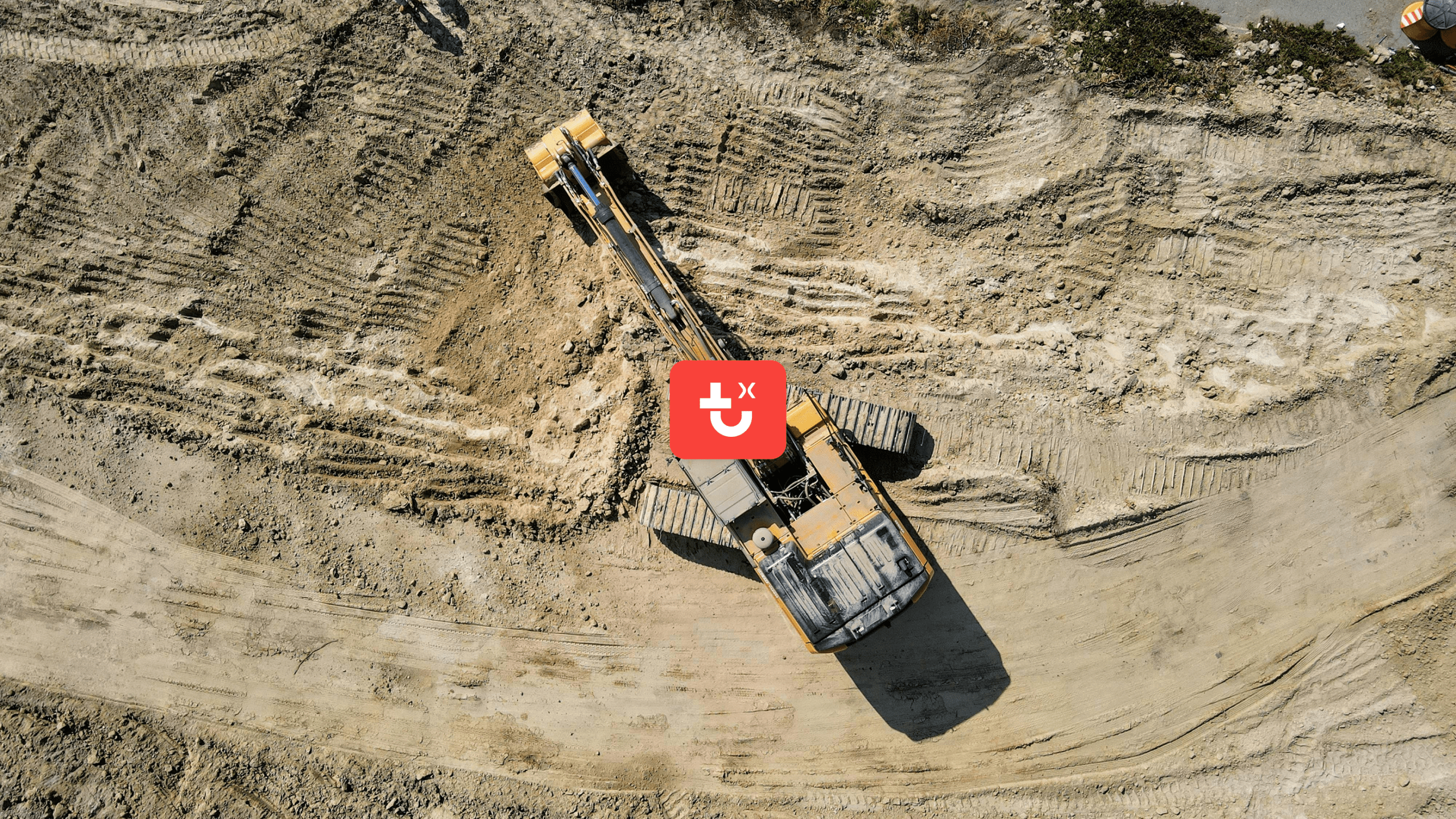 Aerial view of a yellow excavator digging at a construction site with visible tire tracks and rough terrain, highlighting fleet management.