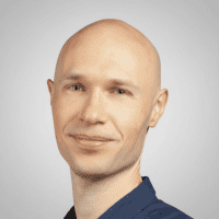 A smiling bald man with fair skin in a dark blue collared shirt, pictured on a light gray background, representing telematics.