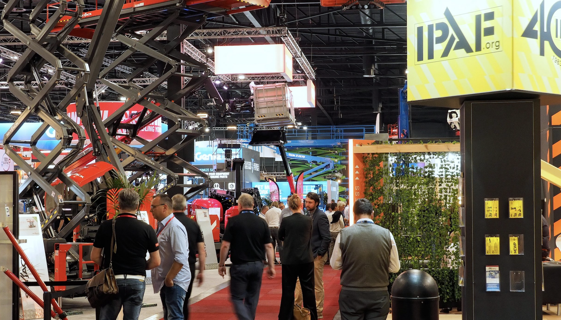 Attendees walk through a busy trade show hall with booths, machinery, and signage, exploring exhibits on construction equipment tracking.