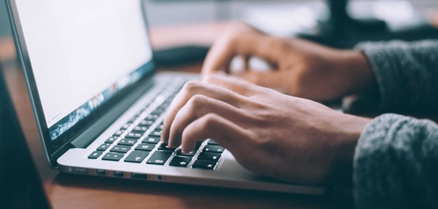 A person types on a laptop keyboard indoors, focused on work—possibly researching construction IoT or technical topics.