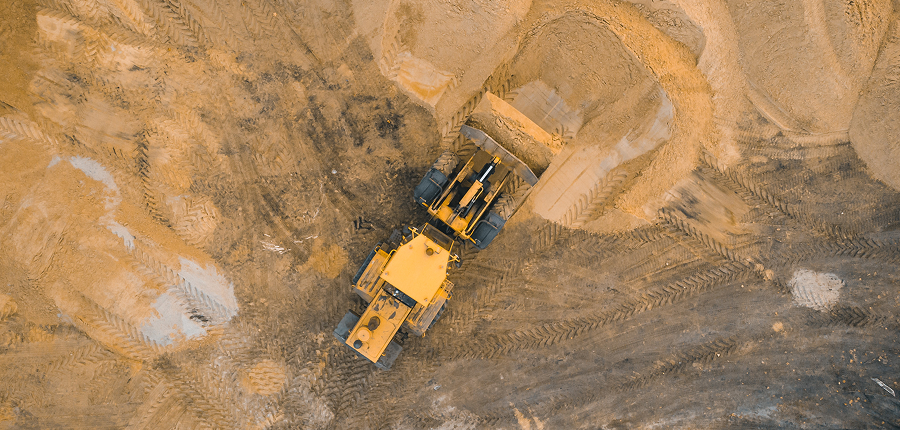 Aerial view of a yellow bulldozer moving sand at a construction site, with visible tire tracks—construction equipment tracking.