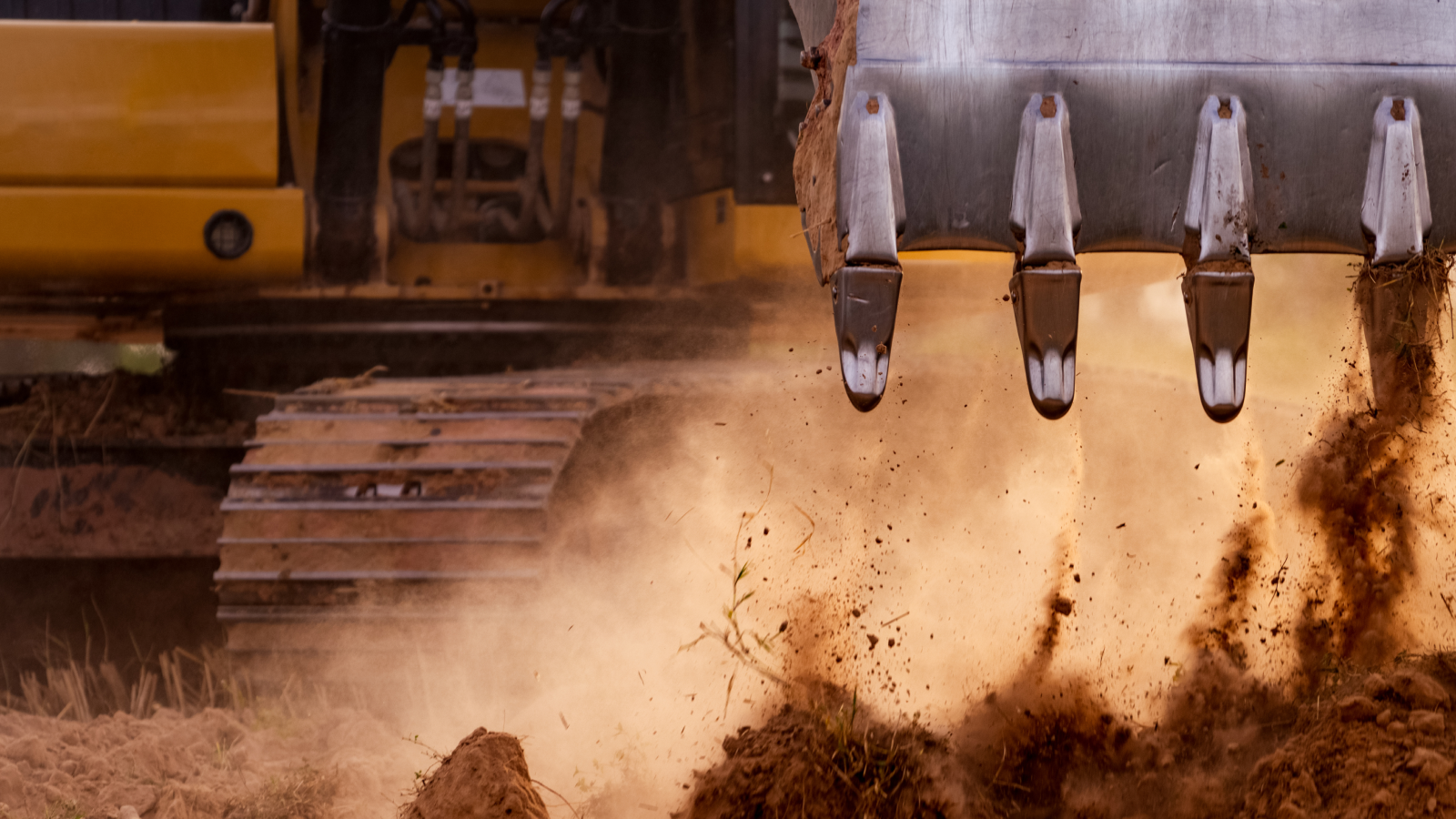 Close-up of an excavator bucket digging into the ground, dirt flying, with metal tracks behind—showing construction IoT in action.
