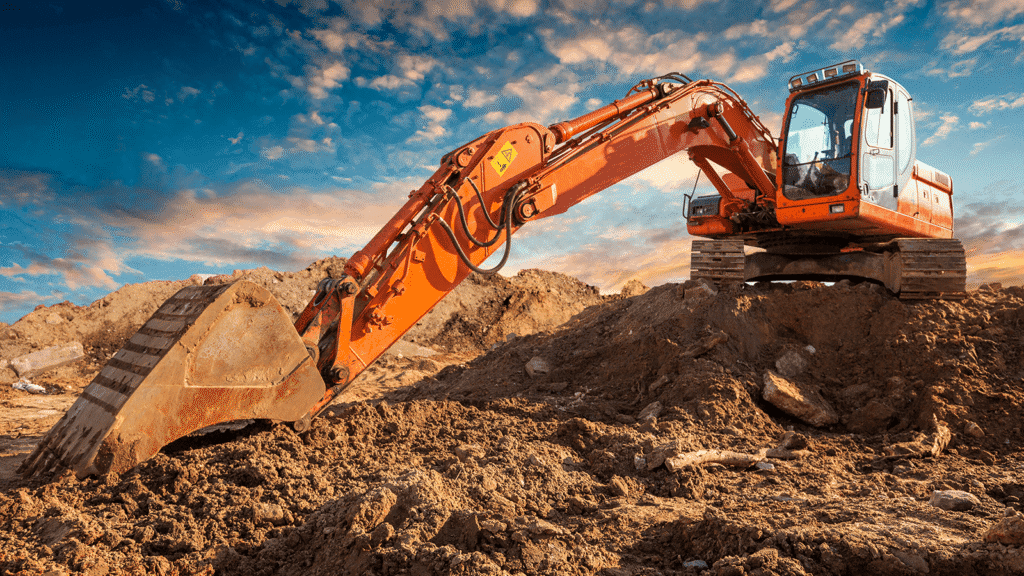 An orange excavator digs into a dirt mound at a construction site beneath a colorful sky, illustrating connected jobsite technology.