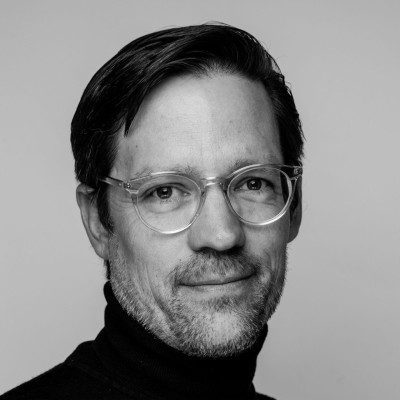 Black and white portrait of a man with glasses and a slight smile, at the Downtime Summit, plain background, construction IoT.