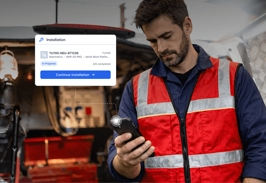 A man in a red safety vest uses his smartphone at a worksite, with an installation progress overlay, illustrating connected jobsite.
