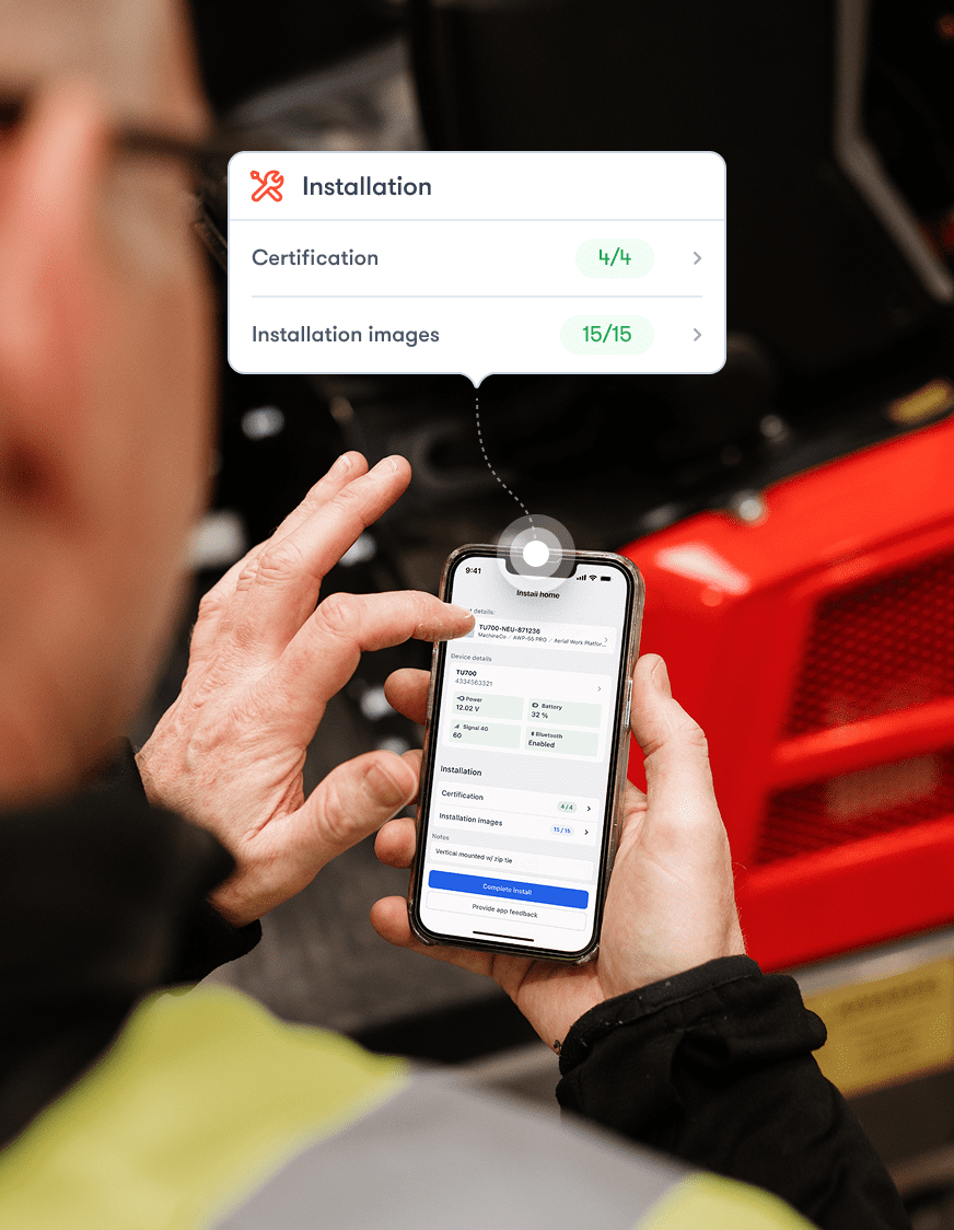 Worker in hi-vis vest checks completed installation checklist on phone by red machine; overlay shows task progress. Construction IoT.