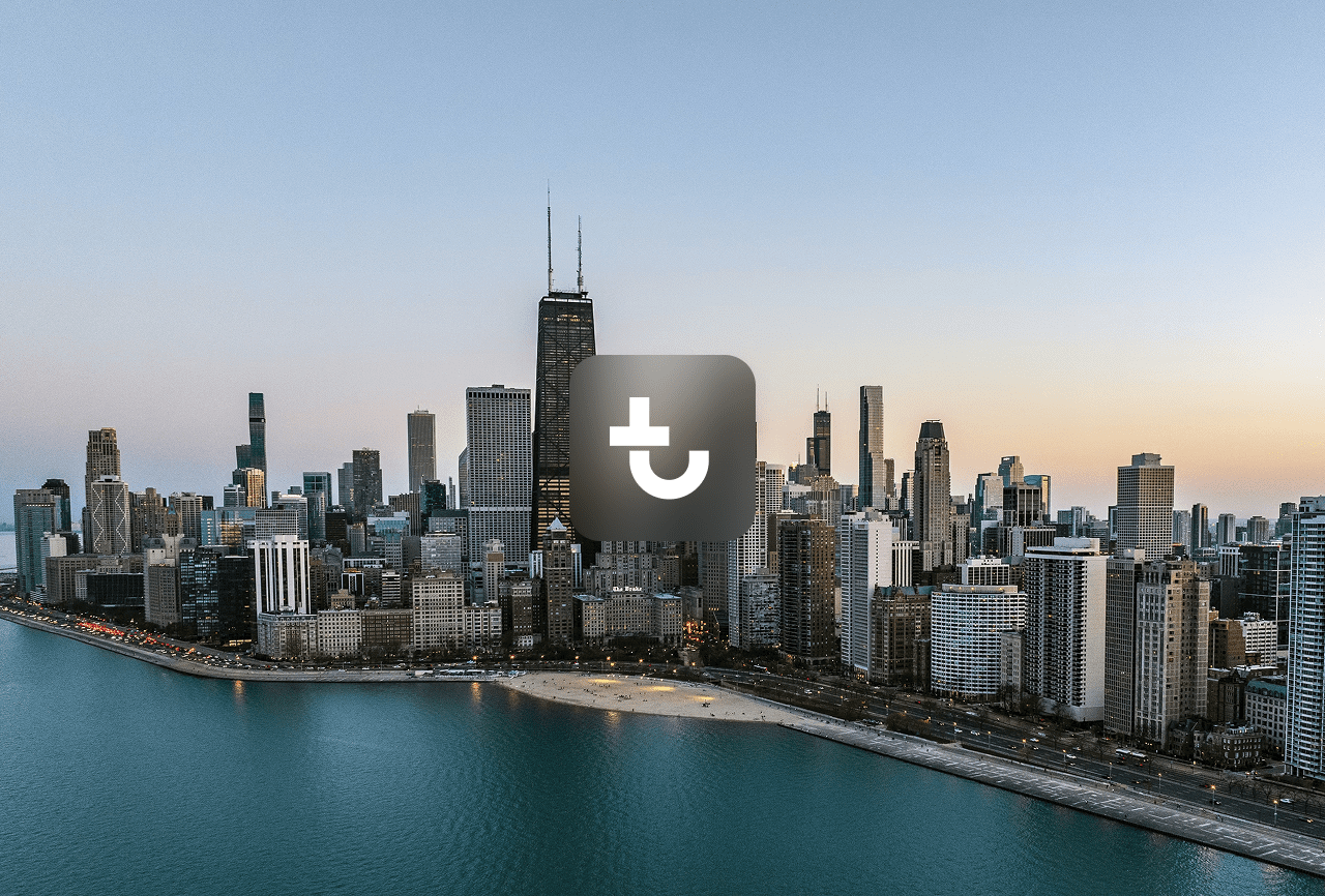 Aerial view of Chicago’s skyline at dusk with a dark square icon centered, highlighting the city for Downtime Summit.