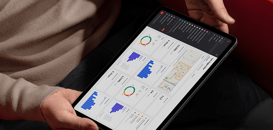 A person holds a tablet with a dashboard showing charts, graphs, and a floor plan, related to construction equipment tracking.