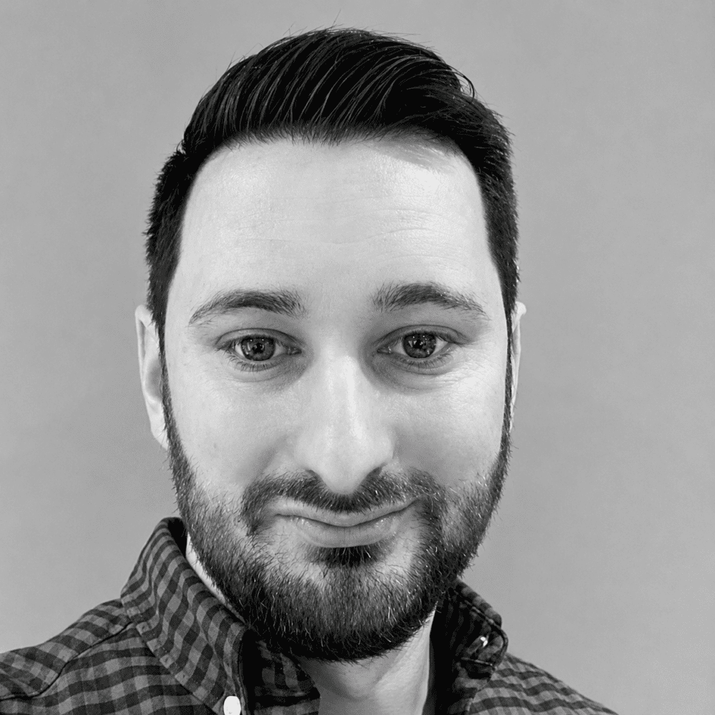 A man with short dark hair and a trimmed beard in a checkered shirt smiles at the camera, suited for a connected jobsite feature.