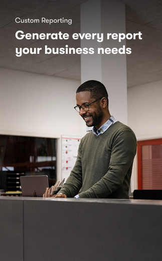 A man in glasses and a green sweater smiles while using a laptop at a desk. Text reads, Custom Reporting—ideal for fleet management.