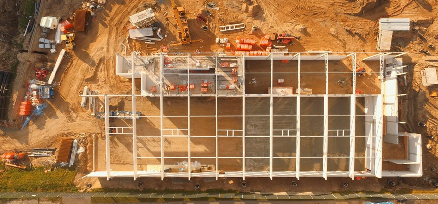 Aerial view of a construction site with steel framework, materials, equipment, and vehicles on sandy ground, highlighting a connected jobsite.