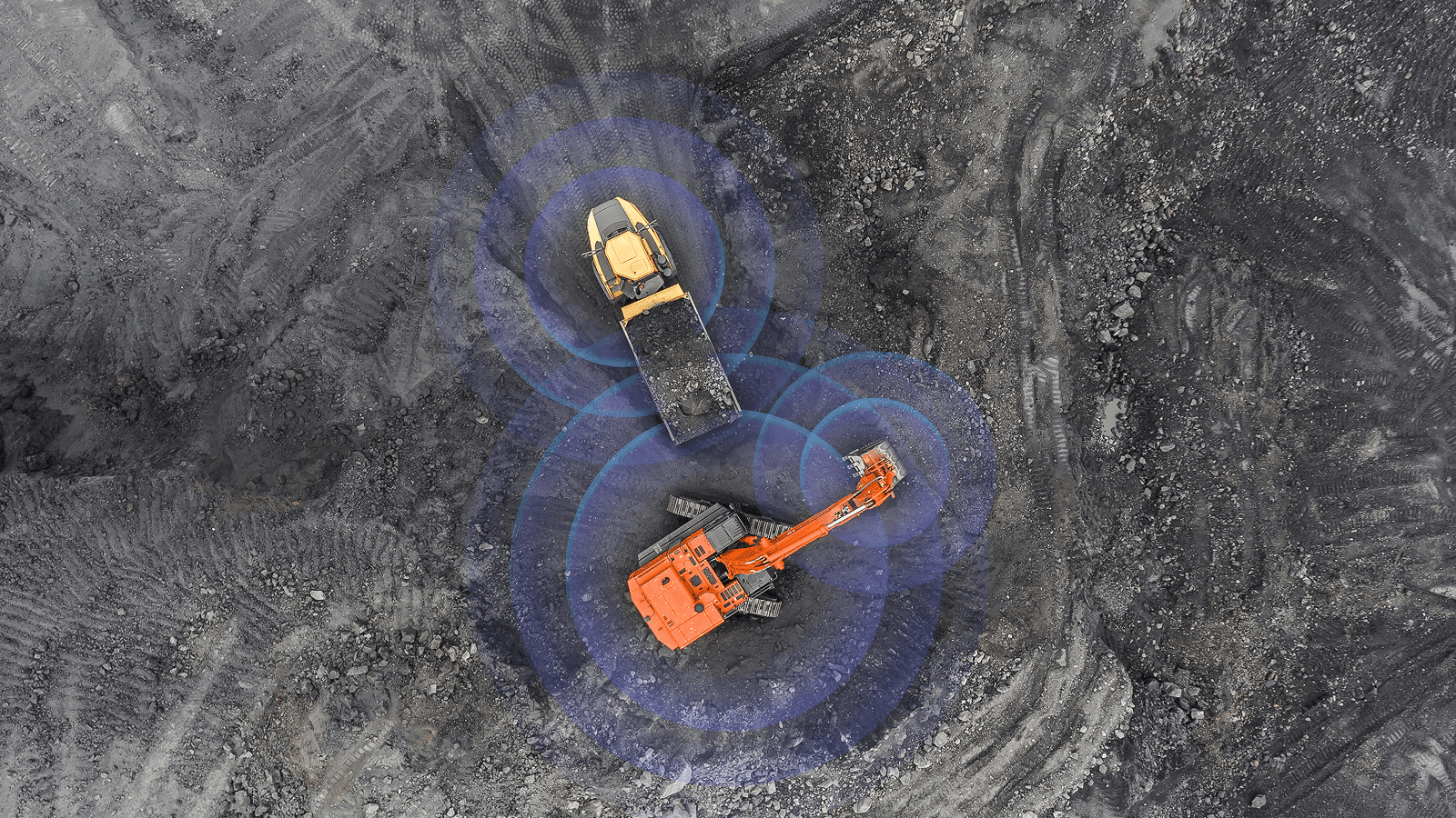 Aerial view of an excavator loading a dump truck at a construction site, with blue circles showing connected jobsite technology.