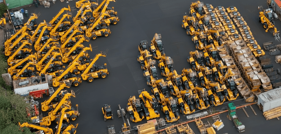 Aerial view of yellow construction vehicles like cranes and forklifts arranged in rows on a lot, with pallets—fleet management.