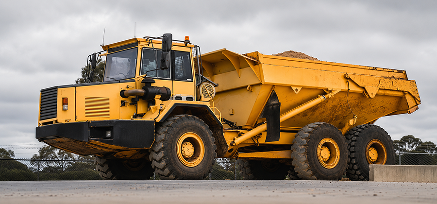 A large yellow dump truck filled with sand is parked on concrete under a cloudy sky, useful for construction fleet management.
