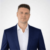 A man in a navy suit and white shirt stands against a plain white background, facing the camera—ideal for a connected jobsite profile.