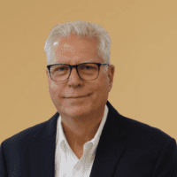A man with short gray hair and glasses in a dark blazer and white shirt smiles slightly, related to construction equipment tracking.
