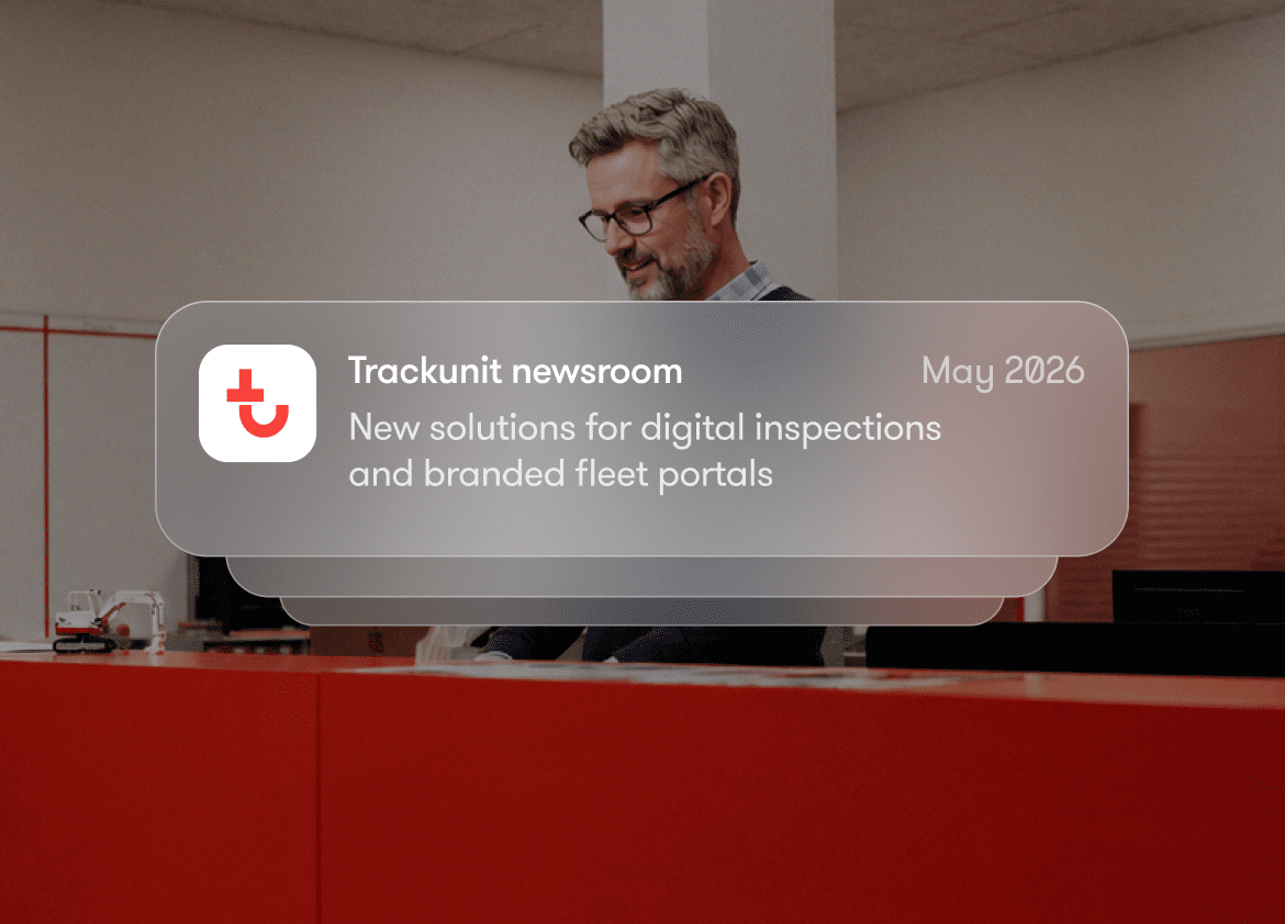A man with gray hair and glasses stands behind a red counter. Onscreen: Trackunit newsroom, May 2026—new telematics solutions.