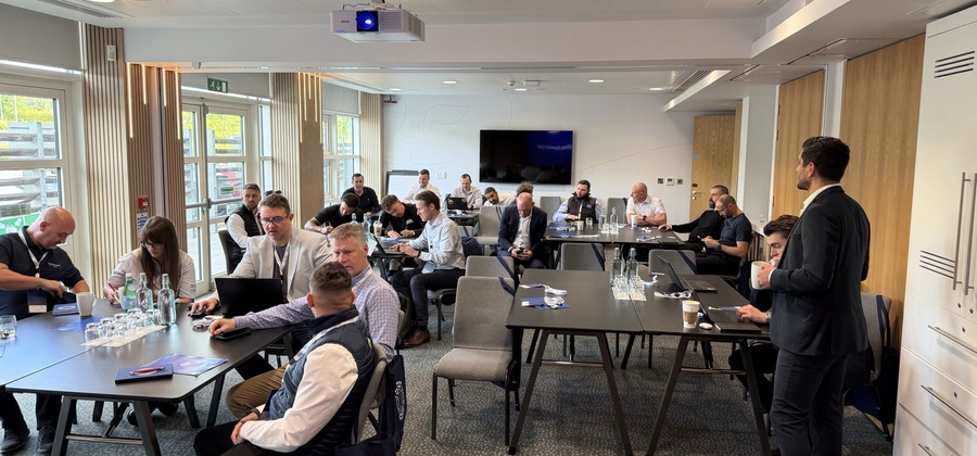 Business professionals in a modern conference room discuss connected jobsite topics, with laptops and water bottles on the tables.
