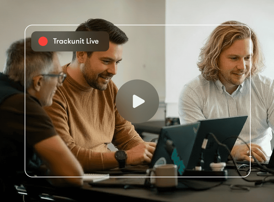 Three people collaborating at laptops during a Trackunit Live session, with a video play button overlay for construction IoT.