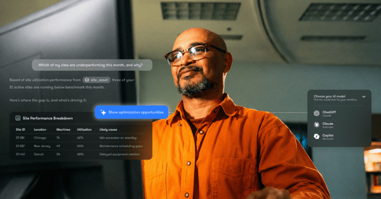 A man in an orange shirt stands in an office, viewing a digital dashboard with site data and optimization tools for a connected jobsite.