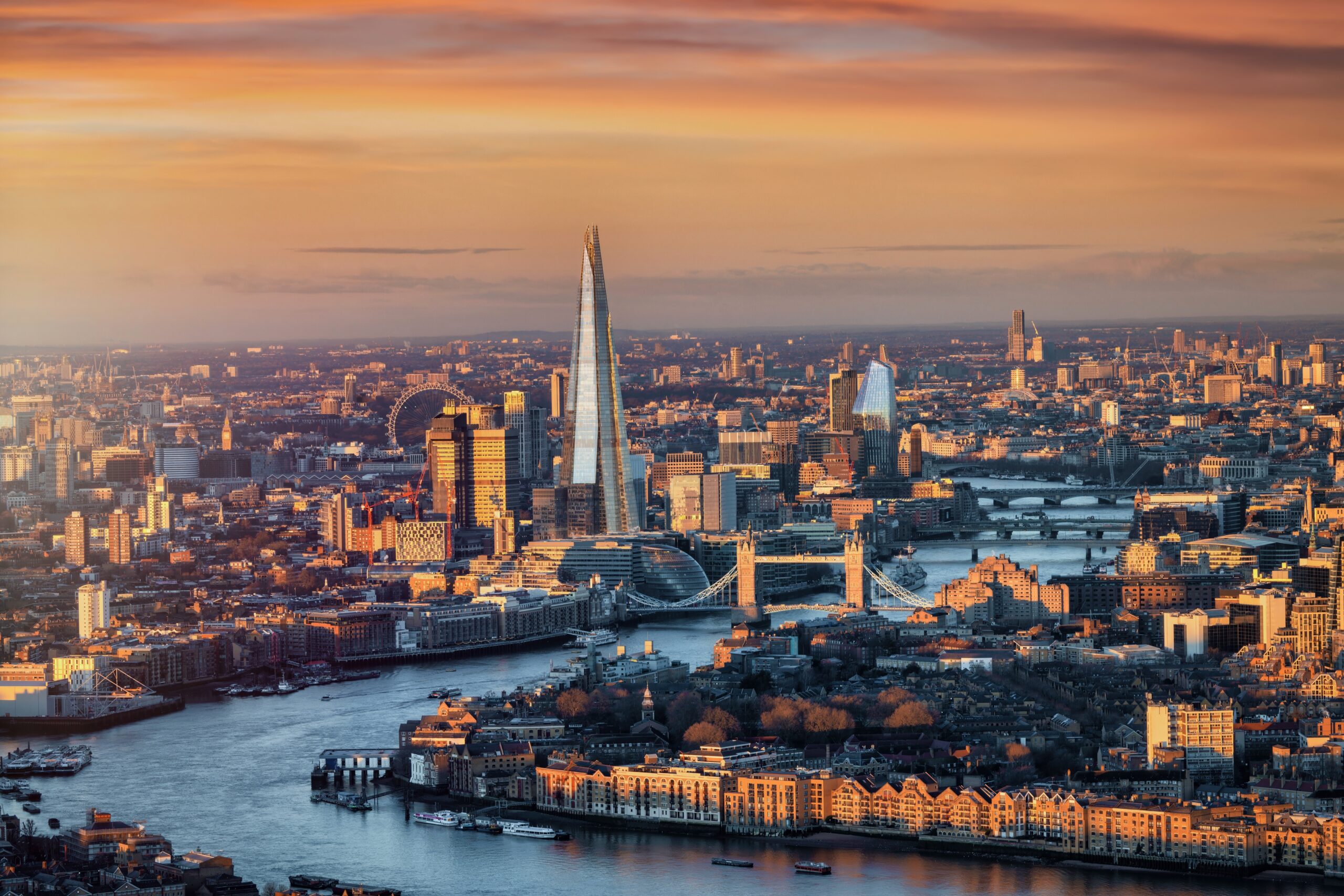 Aerial view of London at sunset, showing the Shard, Tower Bridge, and the River Thames winding through the city under a vibrant orange sky—a glimpse of a skyline set to transform with IPAF elevation UK 2026 initiatives in connected jobsite development.