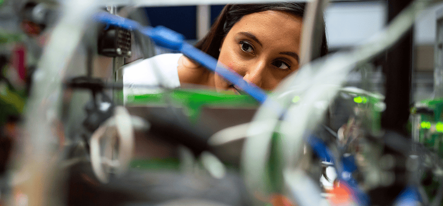 A person closely examines electronic equipment and wires in a technical setting, possibly analyzing fleet management systems for optimal performance.